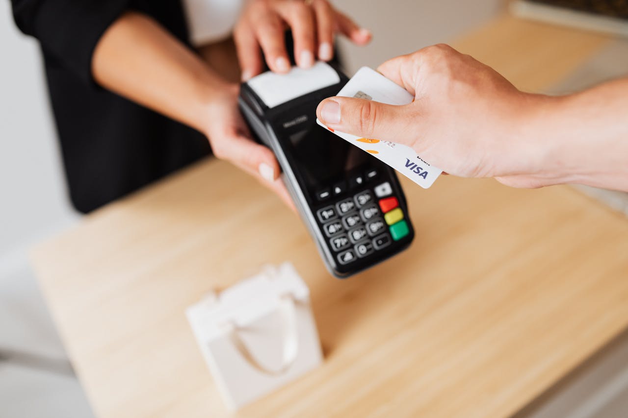 services-06 Close-up of hands using a contactless payment terminal with a credit card indoors.